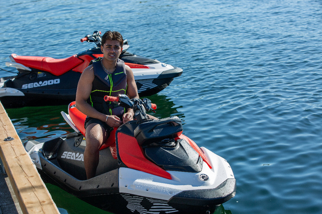 Man sitting on sea doo jet ski on a lake with another jet ski behind