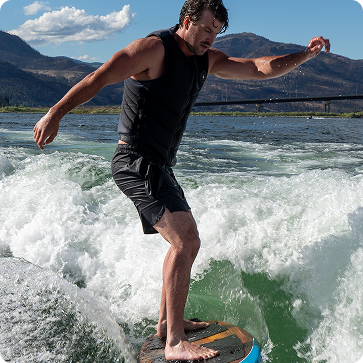 Man wakeboarding on a wave with mountains in the background
