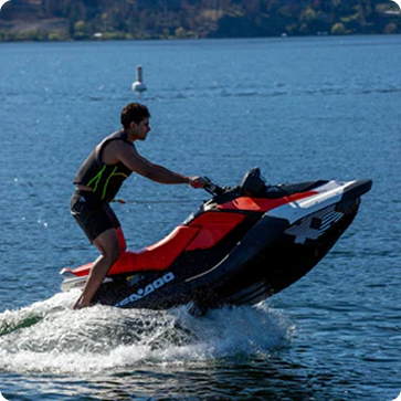 Person riding a Sea-Doo watercraft on a lake with a scenic background
