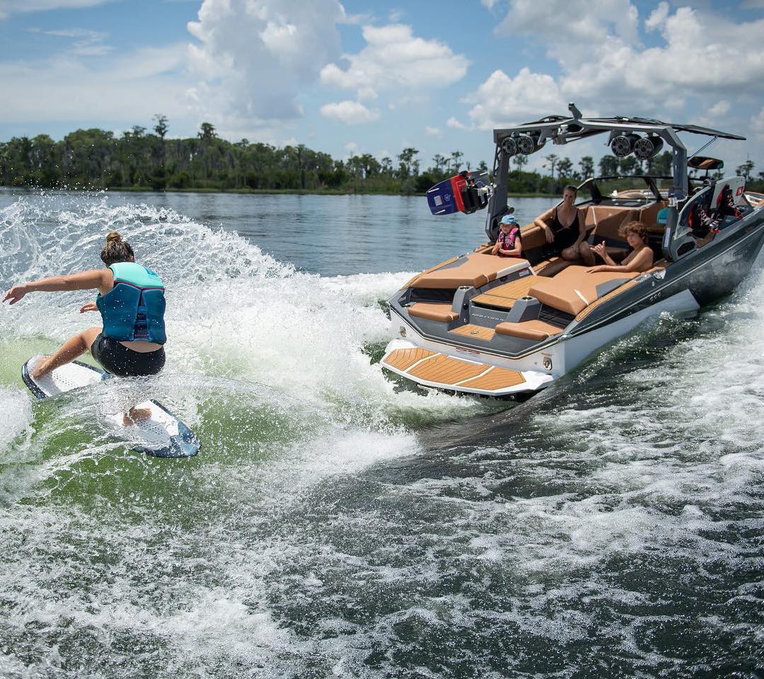 Girl wakesurfing on a wave behind a boat on the lake.